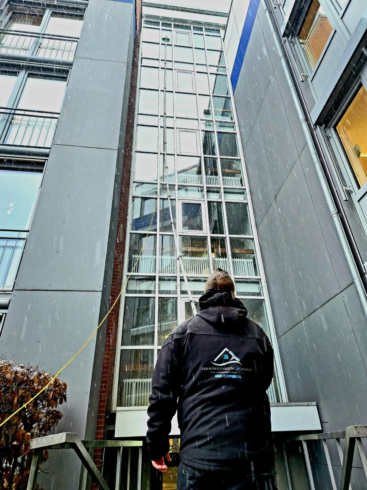 Mitarbeiter der Gebäudereinigung Hübner reinigt eine hohe Glasfassade mit Teleskopstange